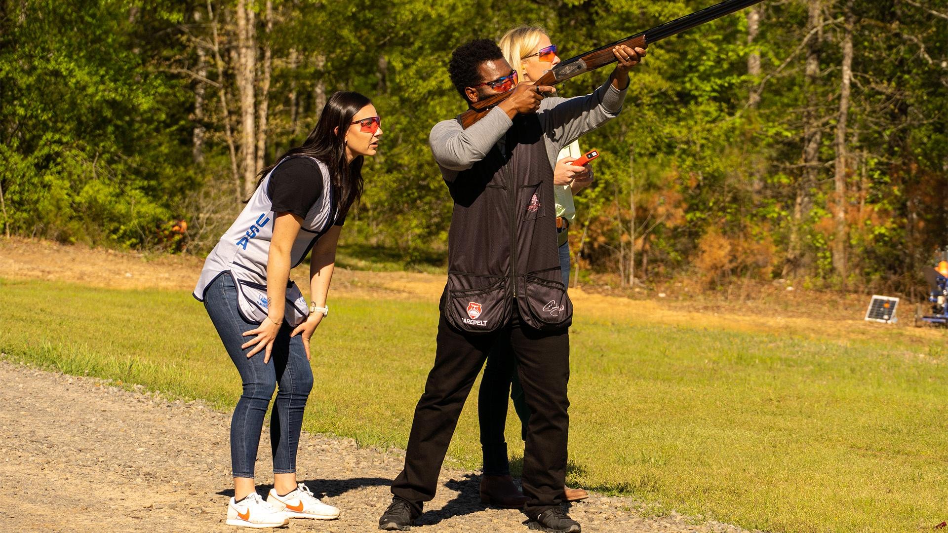 Baratunde aiming a gun with two people behind him