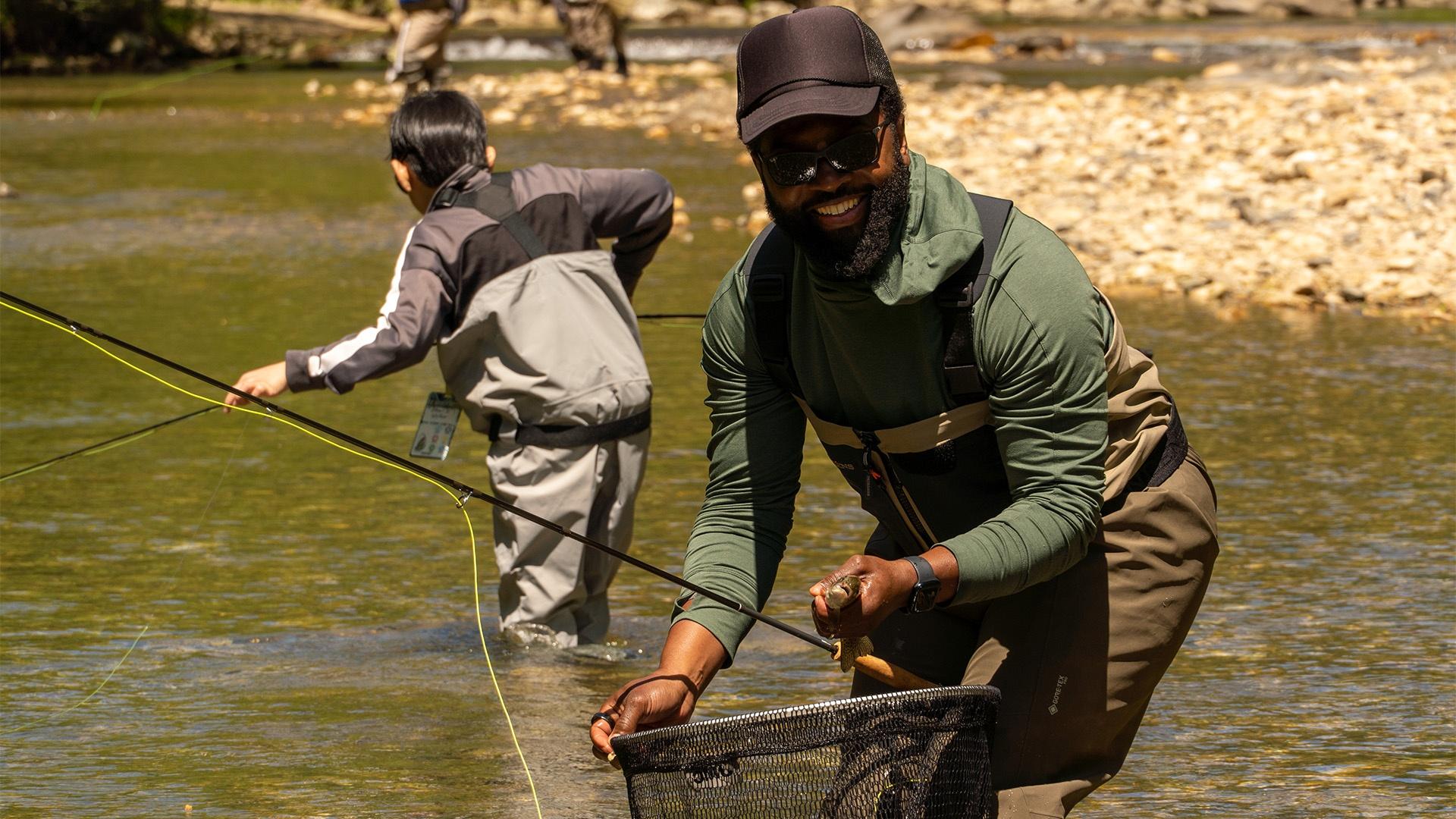 Baratunde holding net while fly fishing with child in background