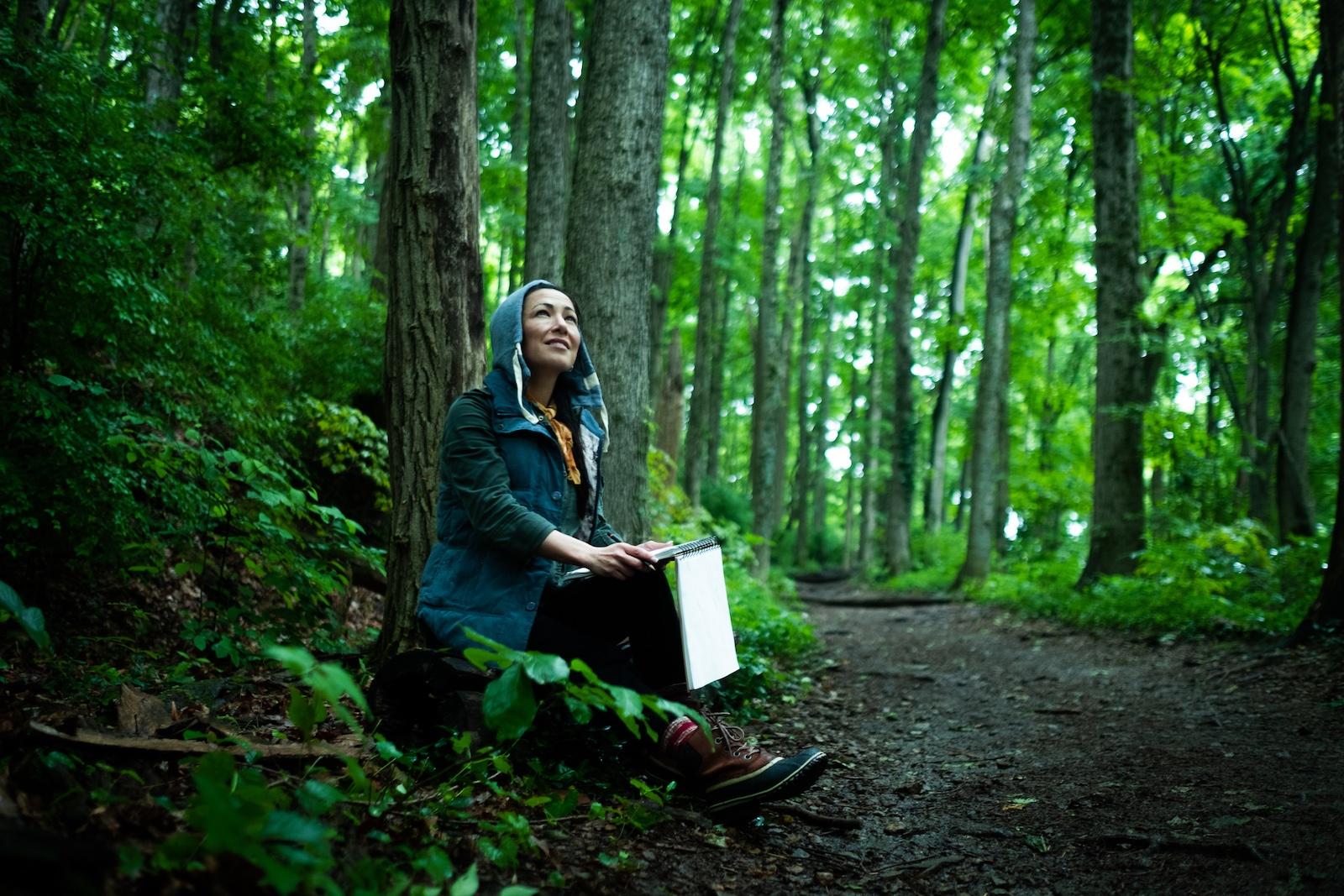 Woman sketches in her journal in the woods